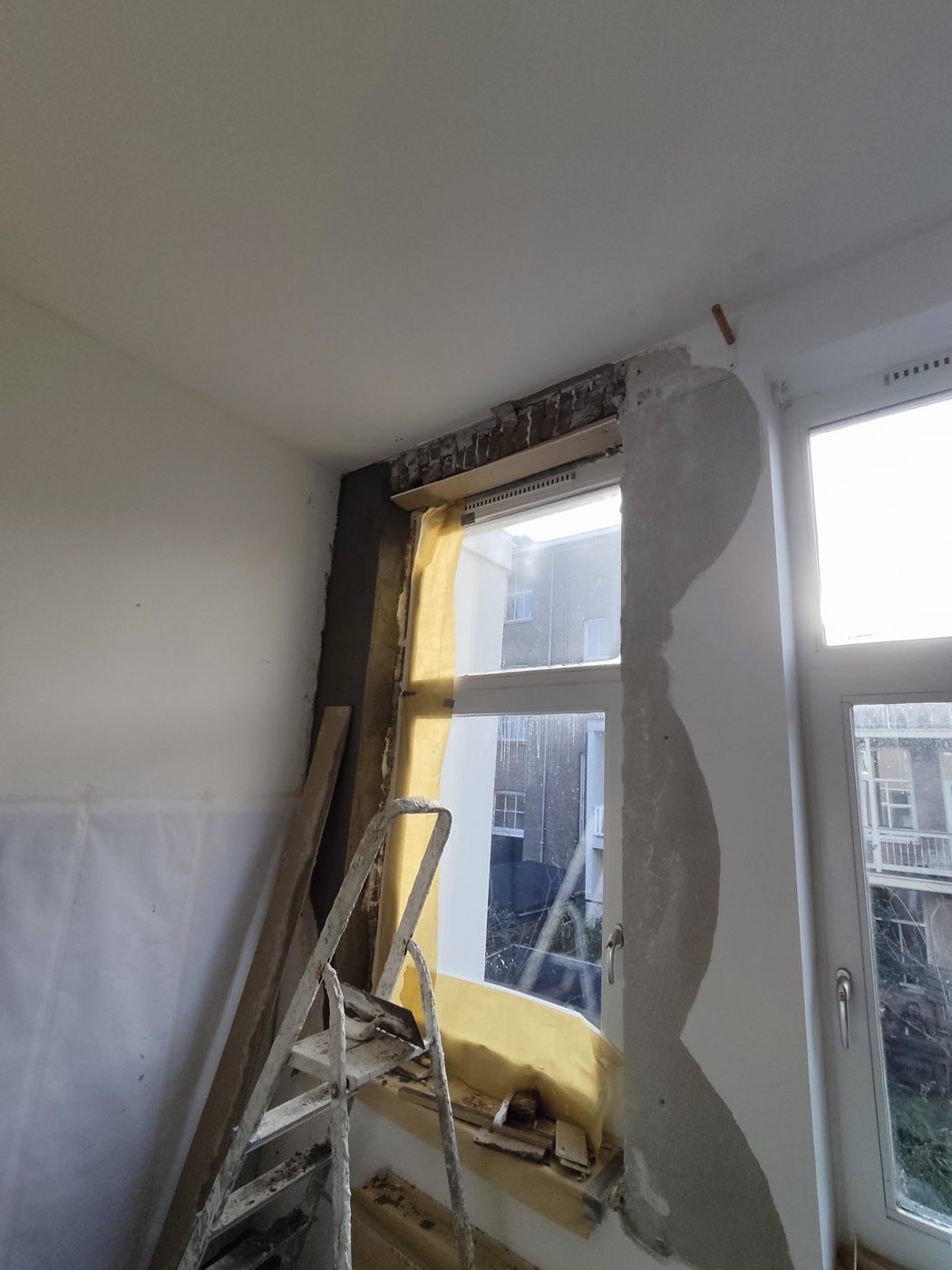 Nieuw stucwerk rond een raamkozijn, met afplakfolie en een trapje