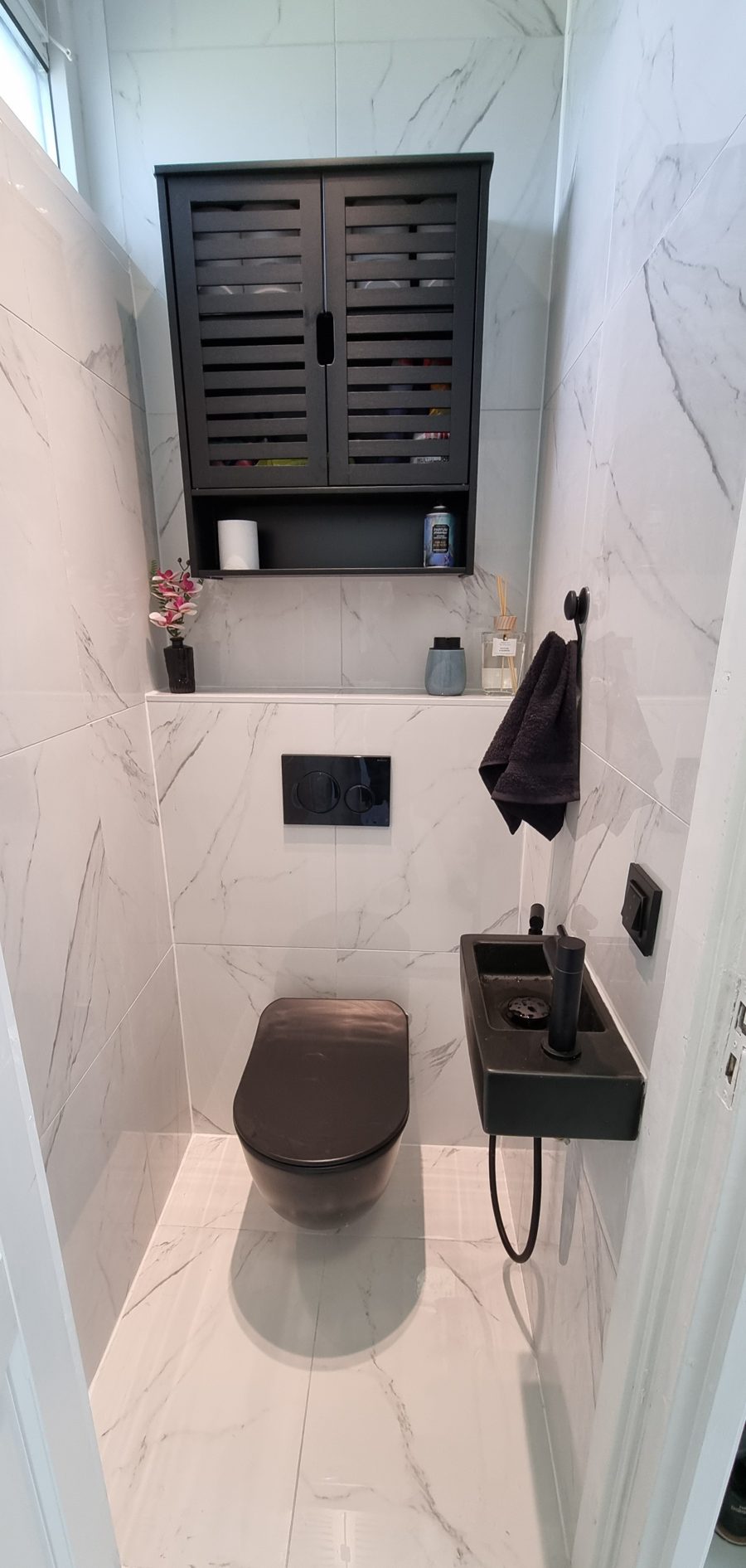 Toilet met witte wandtegels in marmerlook, zwart hangtoilet en een zwart fonteintje