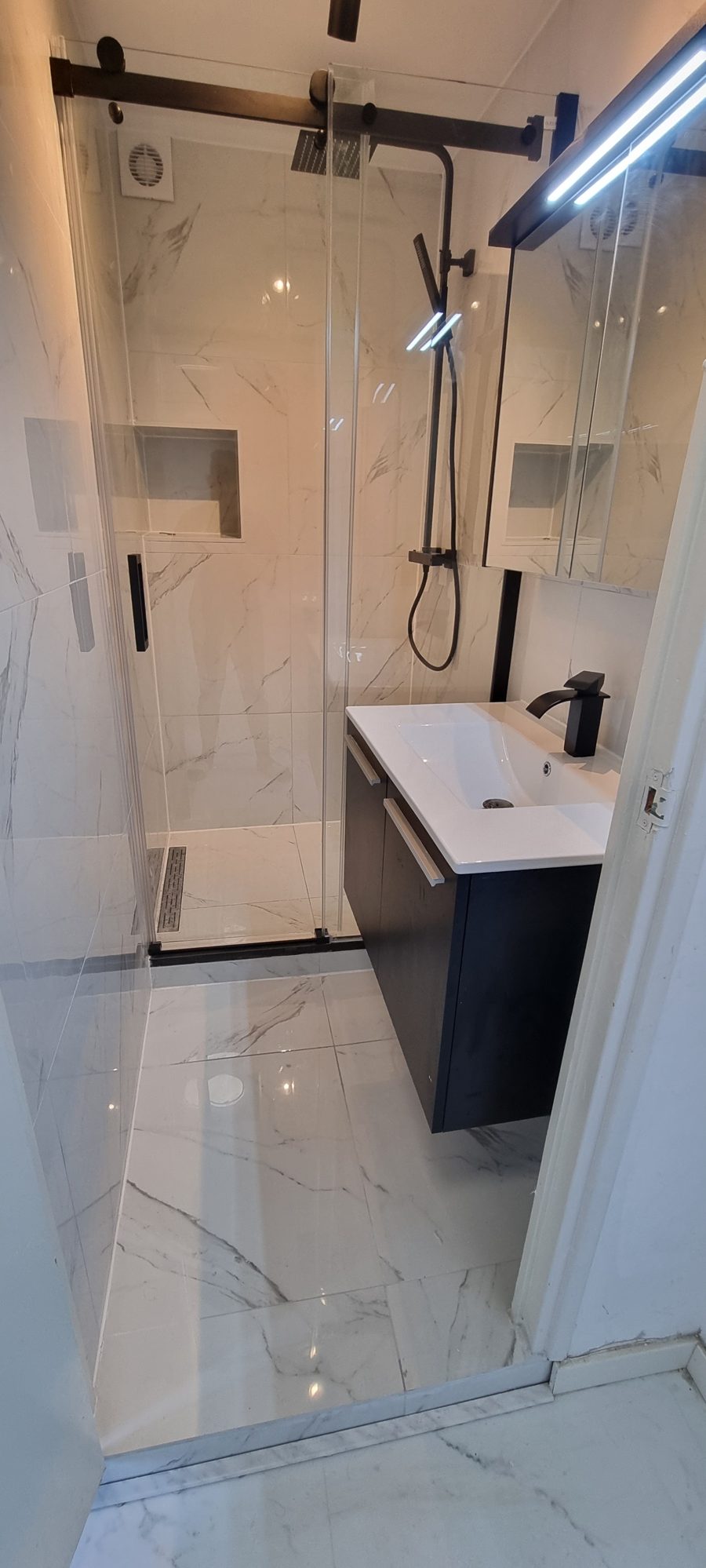Nieuwe douche met witte tegels in marmerlook, zwarte schuifdeur en een zwart badmeubel
