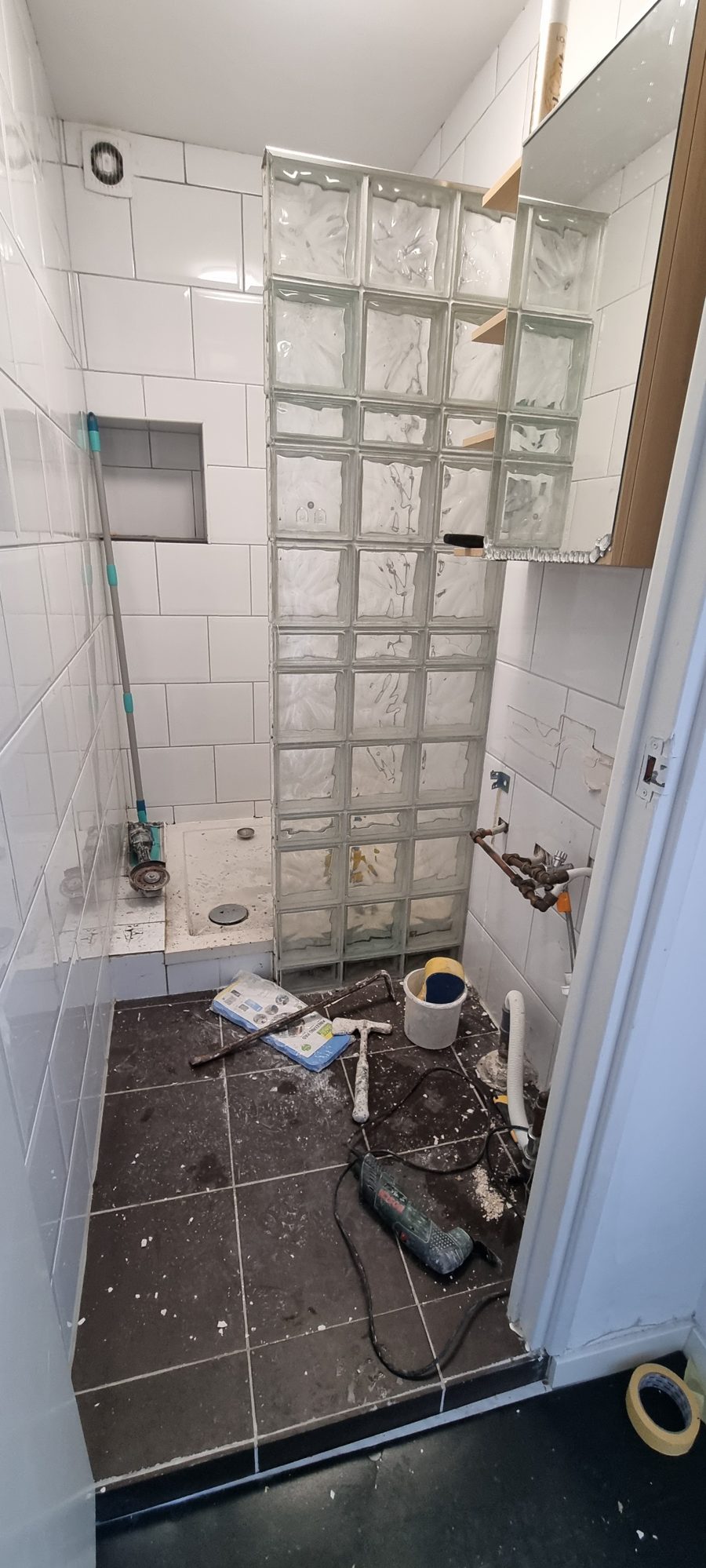 Badkamer tijdens de sloop: oude witte tegels, een wand van glazen bouwstenen en gereedschap op de vloer